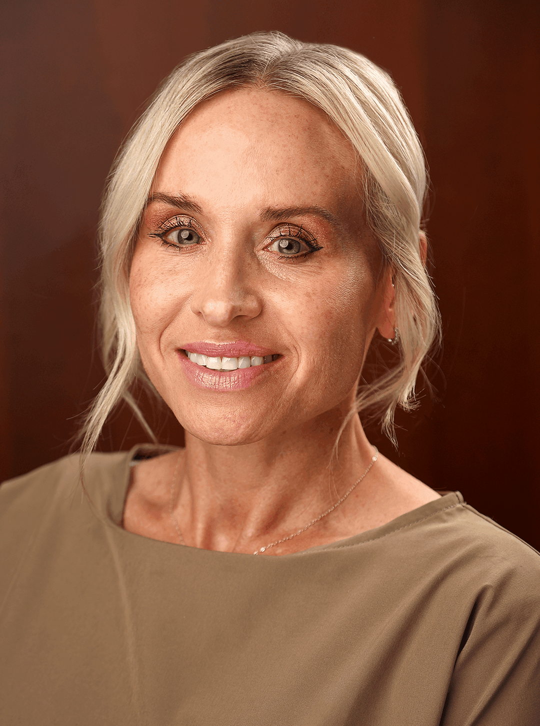 Person with light blonde hair, tied back, wearing a simple beige top and a delicate necklace.